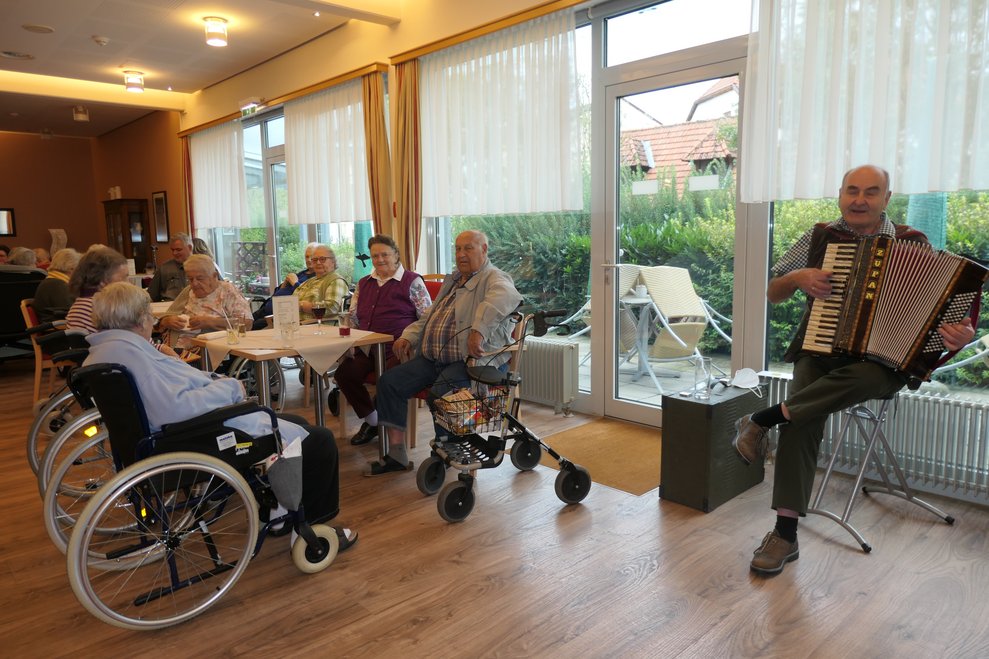 Der Musiker mit Ziehharmonika und im Hintergrund die Gesellschaft.