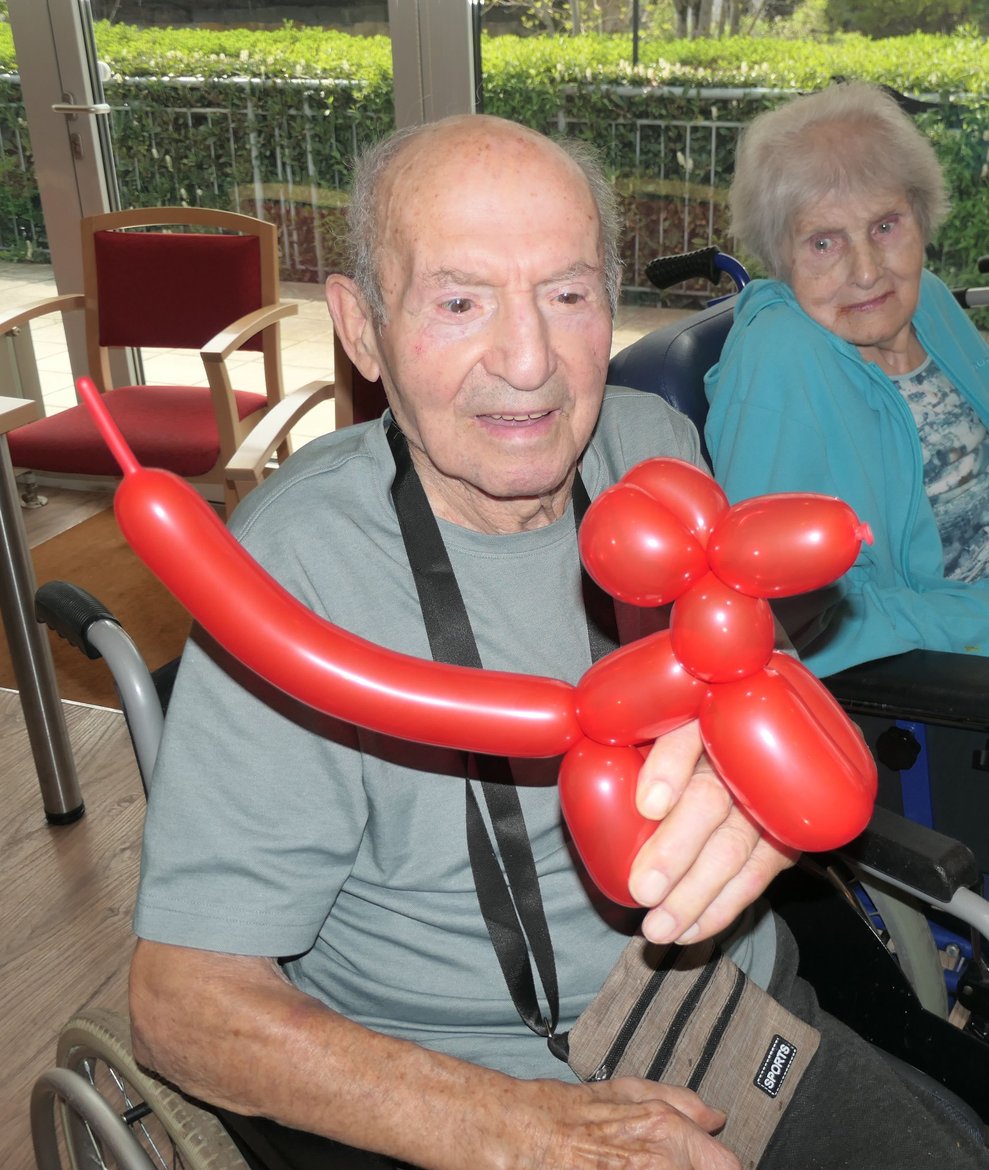 Ein Herr hält einen roten Luftballonhund in die Kamera.