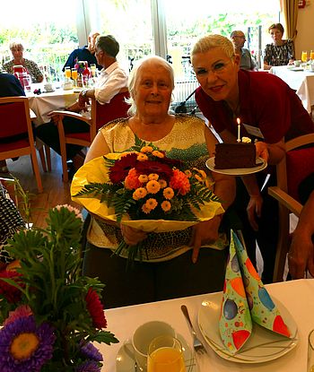 Zwei Damen mit Torte und Blumen.